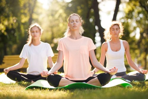 Group of young women practicing yoga, morning meditation in nature at the park.
