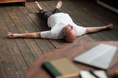 Man meditating on floor Senior caucasian man meditating on a wooden floor of living room and lying in Shavasana pose after practice. Yoga relax, meditating concept, close up