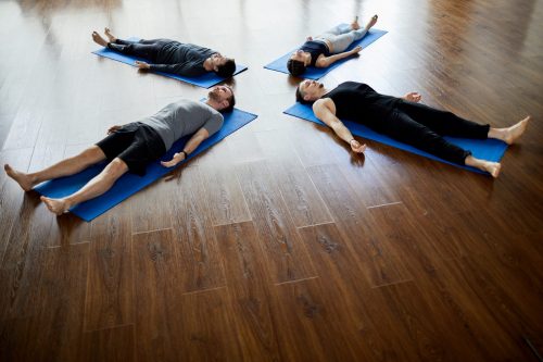 Group of relaxed young people lying on mats in circle and doing savasana while napping at end of yoga practice