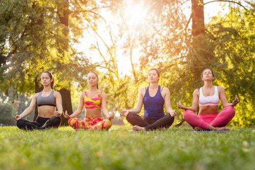 Four beautiful female friends meditating in the park.