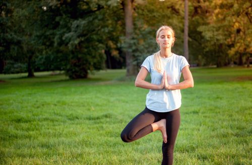 Yoga in the park, young woman doing tree pose vrksasana Yoga in the park, young woman doing tree pose vrksasana