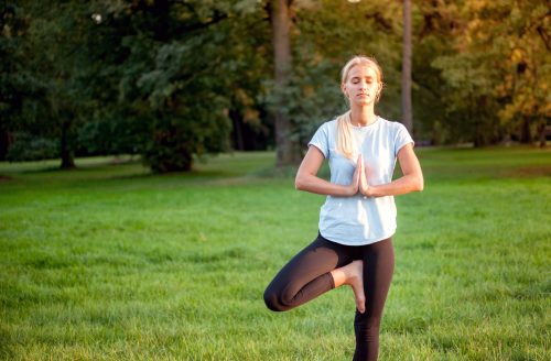 Yoga in the park, young woman doing tree pose vrksasana